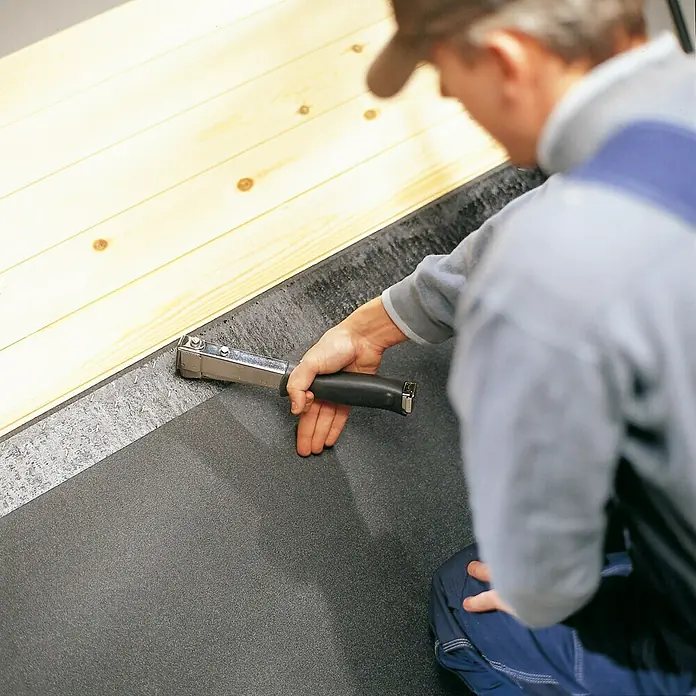 Rapid Hammertacker R11 - Klammertiefe: 6 mm - 10 mm, Geeignet für: Flachdrahtklammern Nr. 140, Verpackung: Blisterpack - Ein Handwerker befestigt mit einem Hammertacker eine Dachpappe an einer Holzkonstruktion. Das Werkzeug ist gut sichtbar.