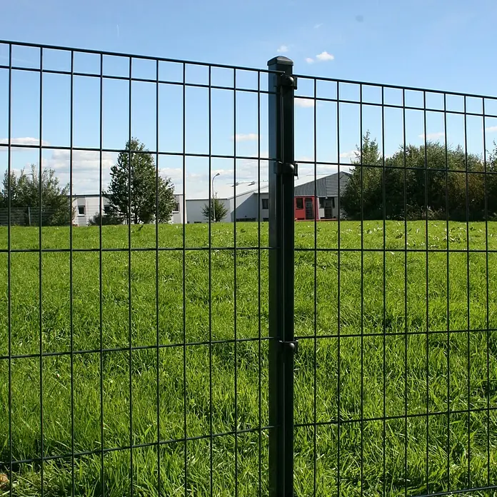 Kraus Zaunpfosten - Höhe: 150 cm, Anthrazit, Metall - Nahaufnahme eines schwarzen Doppelstabmattenzauns, der ein grünes Feld und Gebäude im Hintergrund abgrenzt. Er bietet Sicherheit und Privatsphäre.