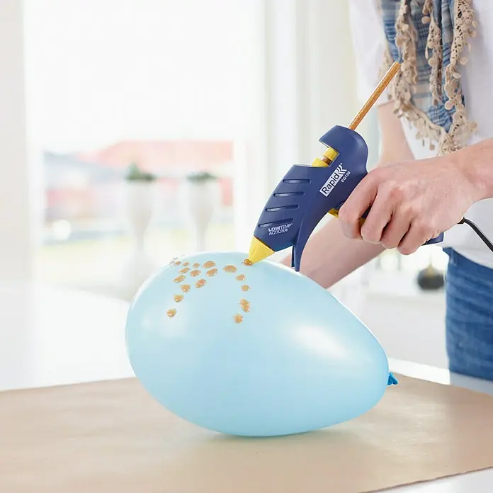 Rapid Heißklebepistole EG 130 LT - Durchmesser Klebepatrone: 9 mm, 130 °C, 100 W - Nahaufnahme einer Person, die mit einer Rapid EG130 Heißklebepistole goldene Klebepunkte auf einen hellblauen Ballon klebt.