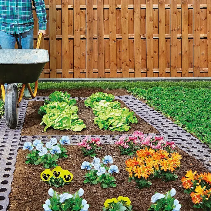 Garantia Beetplatte Maxi - 4 Stk., 70 x 24 cm - Gartenbeet mit Salat, Blumen und einem Schubkarren vor einem Holzzaun. Die Beetumrandung besteht aus Rasengittersteinen.