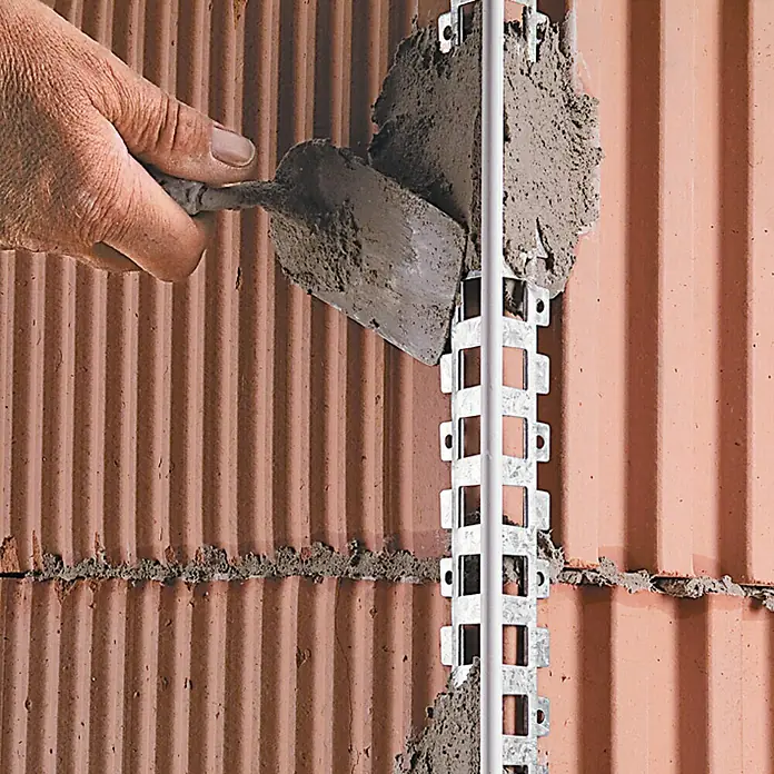 Catnic Putzeckprofil - Länge: 250 cm, Passend für: 10 mm Putzstärke, Stahl, Mit PVC-Kante - Ein Maurer trägt mit einer Kelle Mörtel auf ein Putzprofil auf, das an einer roten Ziegelwand befestigt ist.