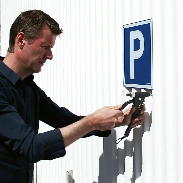 Rapid Blindnietmutter - M 4, 20 Stk. - Eine Person befestigt mit einer Blindnietzange ein blaues Parkplatzschild an einer weißen Wand.