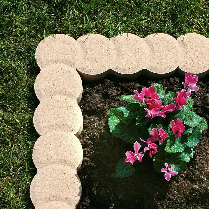 Christoph Mähstein Pali - 22 x 10 x 4,2 cm, Mediterran, Beton - Nahaufnahme eines Gartenbeets mit dekorativen Beetumrandungssteinen und rosafarbenen Cyclamenblüten.