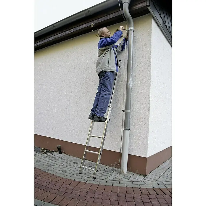 Krause Corda Sprossen-AnlegeleiterArbeitshöhe: 3,2 m, Anzahl Tritte: 8 Stk., Aluminium - Mann auf einer Aluminiumleiter, der am Dach arbeitet, mit Betonpflastersteinen im Vordergrund.
