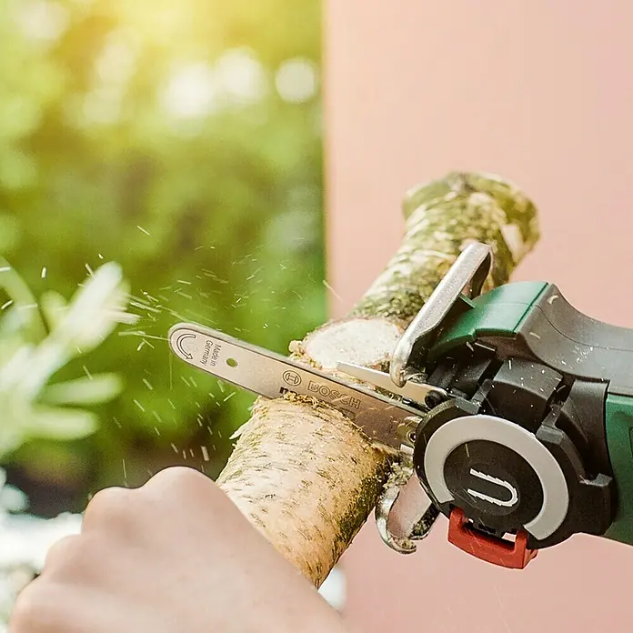 Bosch Power for All 12V NanoBlade-Säge EasyCut 12 - 12 V, 1 Akku, 2 Ah, Leerlaufdrehzahl: 4.100 U/min - Akku-Kettensäge von Bosch in Aktion beim Schneiden eines Astes, Sägespäne fliegen. Kompaktes Design für müheloses Arbeiten.