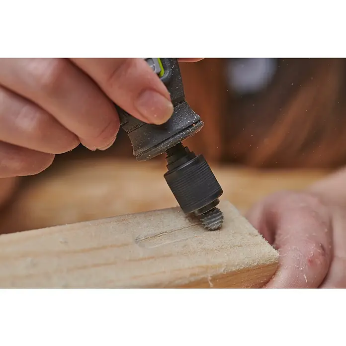 Ryobi Fräser RAR703 - Arbeitsdurchmesser: 9 mm - Ein Werkzeug wird verwendet, um ein Stück Holz zu bearbeiten, wobei Späne fliegen. Das Werkzeug scheint ein Dremel oder ähnliches zu sein.