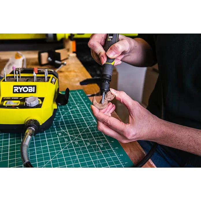 Ryobi Schleifstein-Set RAR52-3 - 3 -tlg. - Nahaufnahme einer Person, die mit einem RYOBI-Rotationswerkzeug an einem kleinen Holzstück arbeitet, wobei die Werkzeugaufsätze im Halter aufbewahrt werden.
