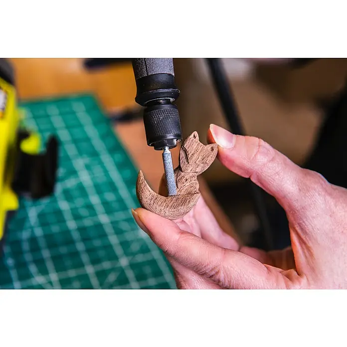 Ryobi Schleifstein-Set RAR52-3 - 3 -tlg. - Nahaufnahme eines Mannes, der mit einem Dremel ein hölzernes Fuchsobjekt bearbeitet. Präzision und Handwerkskunst vereinen sich hier.