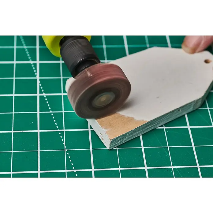Ryobi Fächerschleifer RAR604 - Arbeitsdurchmesser: 30 mm, Körnung: 80 - Schleifwerkzeug mit rotierendem Schleifkopf bearbeitet ein Holzstück auf einer grünen Schneidematte.
