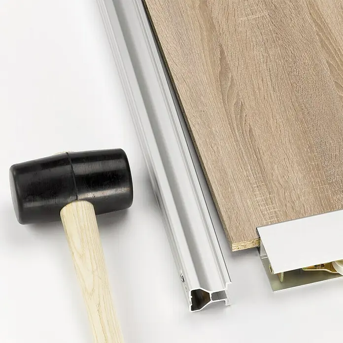 Room Plaza Easy Schiebetür-Bau-Set - Eiche geplankt/Eiche Trüffel, Farbe Beschlag: Silber - Nahaufnahme von Baumaterialien, darunter ein Gummihammer, eine Aluminiumleiste und eine Holzplatte.