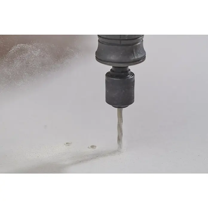 Ryobi Trockenbau-Bohrersatz RAR403-8 - 3,2 mm - Ein Bohrer arbeitet sich durch ein weißes Material, Staubpartikel fliegen herum. Der Bohrer ist grau und der Untergrund erscheint eben und sauber.