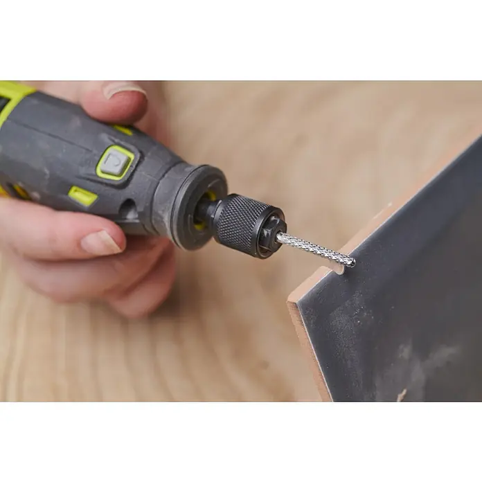 Ryobi Fliesenbohrer RAR405 - Arbeitsdurchmesser: 3,17 mm, Passend für: Rotationswerkzeuge mit 3,2 mm (1/8") Spannzangenkapazität - Eine Nahaufnahme eines Ryobi-Werkzeugs mit rotierendem Bohrer, das zum Bohren eines Lochs in eine dunkle Keramikfliese verwendet wird.