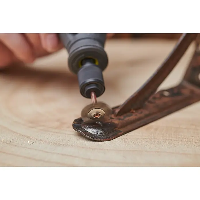 Ryobi Drahtbürsten-Set RAR202-2 - Arbeitsdurchmesser: 17 mm - 19 mm, Passend für: Rotationswerkzeuge mit 3,2 mm (1/8") Spannzangenkapazität - Detailansicht eines Werkzeugs beim Entrosten eines alten Metallstücks auf einer hellen Holzoberfläche.