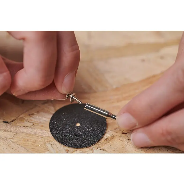 Ryobi Aufspanndorn RAR901Arbeitsdurchmesser: 3,2 mm - Detailaufnahme einer Person, die eine Trennscheibe an einer Spindel befestigt, um sie mit einem Werkzeug zu verwenden.