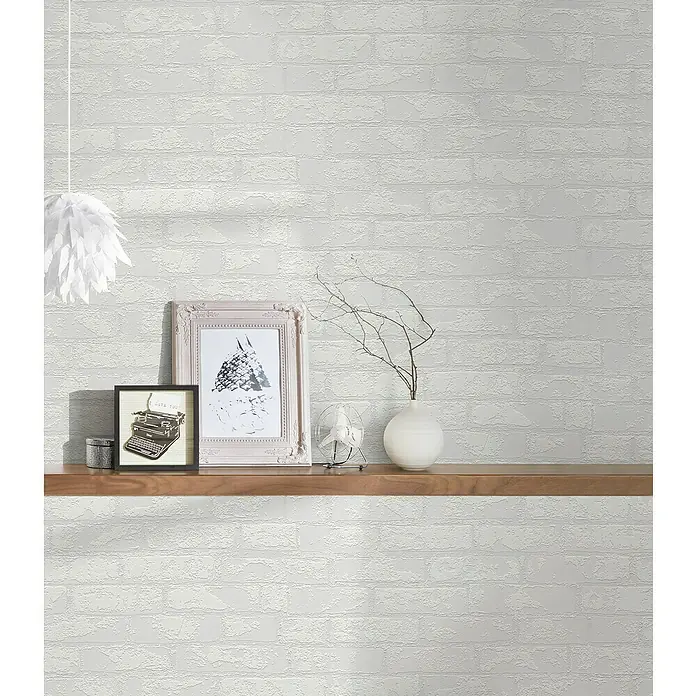 Atlantis Protect Vliestapete Ziegelstein - Weiß, Uni, 10,05 cm x 0,53 m - Nahaufnahme eines Regals mit dekorativen Gegenständen vor einer weißen Ziegelwand mit hängender Lampe.