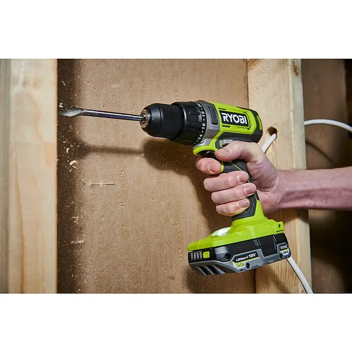 Ryobi ONE+ Maschinen-Set Combo Kit R18CK3G-242 - 18 V, 2 Ah - 4 Ah, 2 Akkus, 6 -tlg. - Nahaufnahme eines Ryobi Akku-Bohrschraubers, der ein Loch in eine Holzwand bohrt, mit Holzspänen, die beim Bohren entstehen.