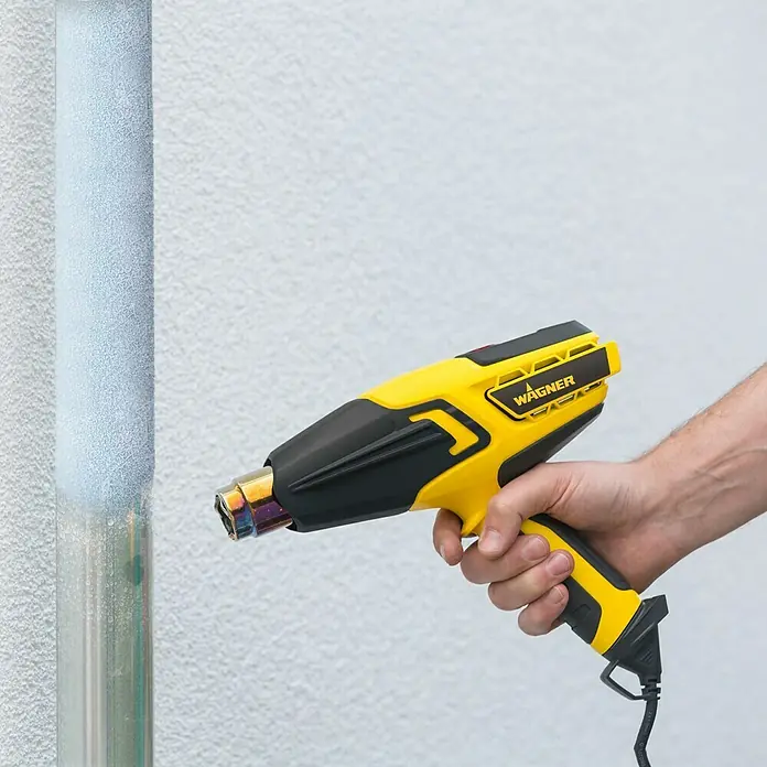 Wagner Heißluftgebläse Furno 500 - Leistungsaufnahme: 2.000 W, Temperaturbereich: 60 °C - 600 °C - Nahaufnahme einer WAGNER Heißluftpistole, die zum Entfernen von Farbe von einem Rohr verwendet wird. Ideal für Renovierungsarbeiten und Heimwerkerprojekte.