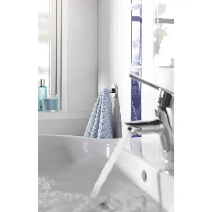 Grohe Essentials Bademantelhaken - Chrom, Glänzend - Nahaufnahme eines Waschbeckens mit laufendem Wasserhahn und einem blauen Handtuch an der Wand.