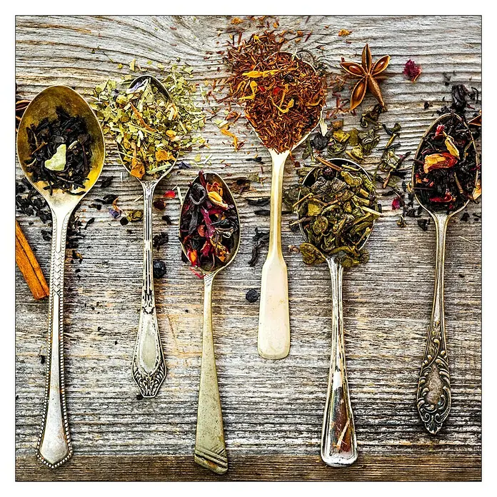 Glasbild - Herbage on Spoon IV, B x H: 50 x 50 cm - Verschiedene Teesorten in antiken Löffeln auf einem Holztisch präsentiert.