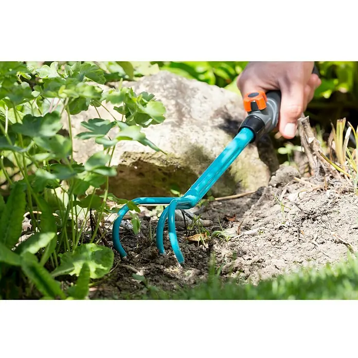 Gardena Combisystem Kleingrubber - Arbeitsbreite: 7 cm, Stahl - Nahaufnahme einer blauen Gartenkralle, die in der Erde verwendet wird, um Beete aufzulockern und zu belüften, gehalten von einer Hand.