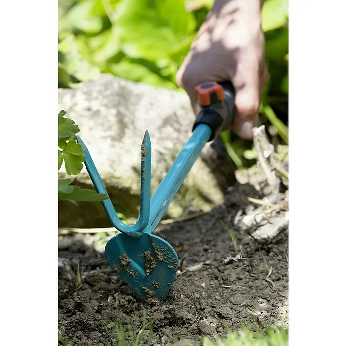 Gardena Combisystem Kleinhacke - Arbeitsbreite: 6 cm, Blattform: Herzförmig, Anzahl Zinken: 2 - Nahaufnahme einer Gartenhacke mit blauem Griff, die in der Erde steckt, ideal zum Auflockern und Jäten von Beeten.