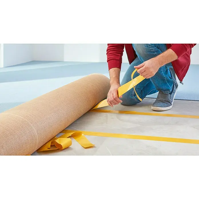 Tesa Verlegeband - 25 m x 50 mm, Beidseitig selbstklebend, Geeignet für: Fußbodenheizung - Ein Mann verlegt einen Teppich mit doppelseitigem Klebeband auf einem sauberen Untergrund. Das gelbe Klebeband ist deutlich sichtbar.