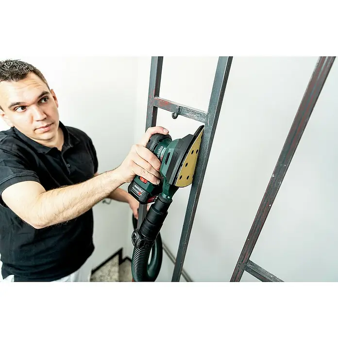 Metabo Akku-Multischleifer PowerMaxx SMA 12 BL - 12 V, Ohne Akku, Breite Schleifplatte: 100 mm, Länge Schleifplatte: 150 mm - Ein Mann schleift eine Metallstruktur mit einem Metabo-Elektrowerkzeug. Das Werkzeug ist grün und hat einen schwarzen Schlauchaufsatz.