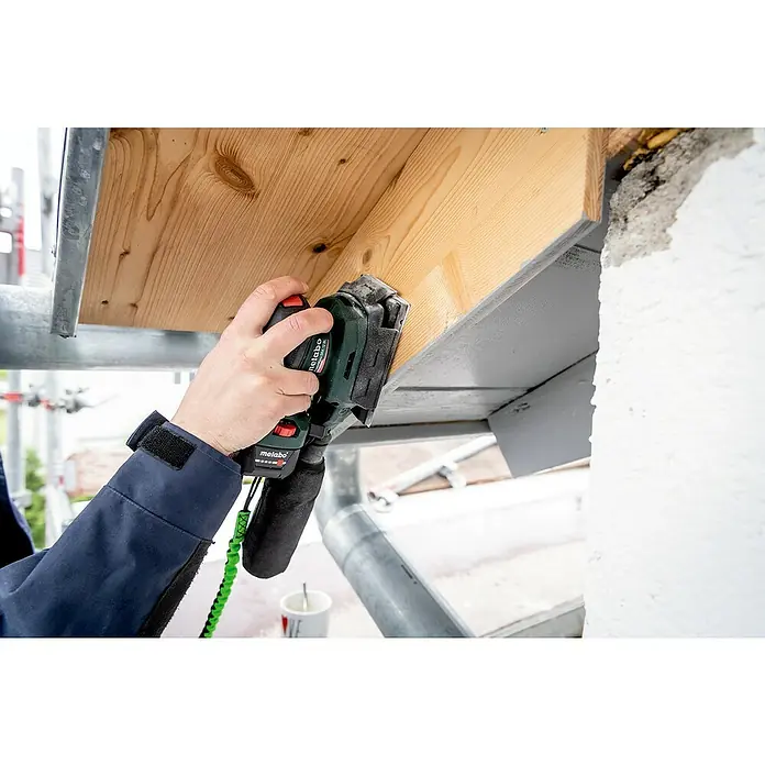 Metabo Akku-Schwingschleifer PowerMaxx SRA 12 BL - 12 V, Ohne Akku, Breite Schleifplatte: 80 mm, Länge Schleifplatte: 130 mm - Nahaufnahme einer Person, die mit einem Metabo-Schleifer an einem Holzstück arbeitet, während sie auf einem Gerüst steht.