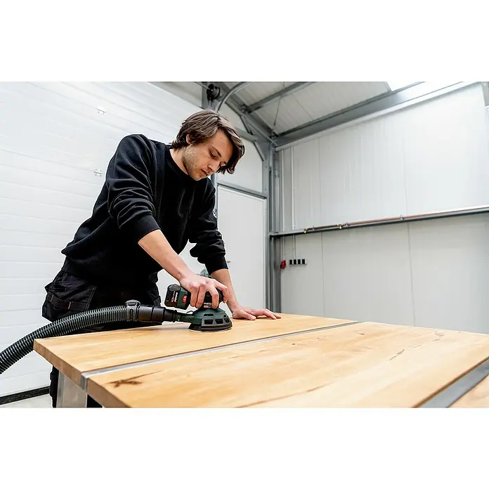 Metabo Akku-Exzenterschleifer PowerMaxx SXA 12-125 BL - 12 V, Ohne Akku - Ein Mann schleift ein Holzbrett mit einem Metabo Exzenterschleifer. Das Gerät ist mit einem Staubsauger verbunden, um Staub zu minimieren.