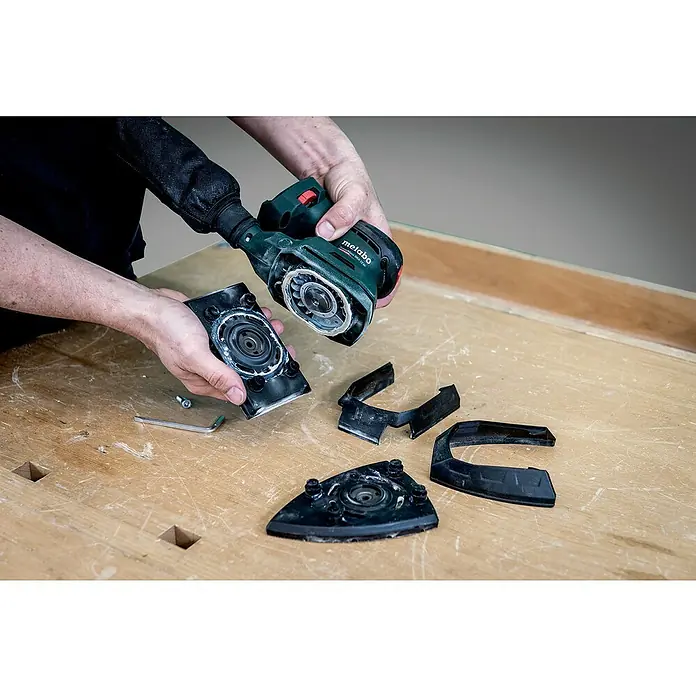 Metabo Akku-Multischleifer PowerMaxx SMA 12 BL - 12 V, Ohne Akku, Breite Schleifplatte: 100 mm, Länge Schleifplatte: 150 mm - Ein Metabo-Multischleifer wird in seine Einzelteile zerlegt und auf einem Werktisch präsentiert.