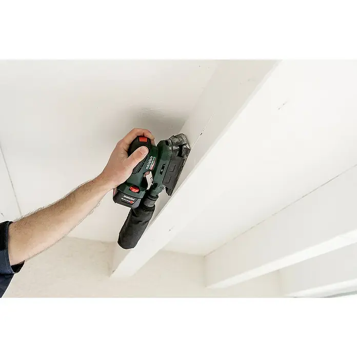 Metabo Akku-Schwingschleifer PowerMaxx SRA 12 BL - 12 V, Ohne Akku, Breite Schleifplatte: 80 mm, Länge Schleifplatte: 130 mm - Ein Mann schleift mit einem Metabo-Multischleifer eine weiße Deckenleiste, Staub wird abgesaugt. Das Gerät ist kabellos und handlich.