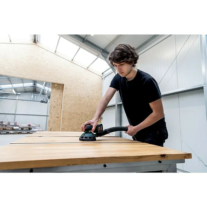 Metabo Akku-Exzenterschleifer PowerMaxx SXA 12-125 BL - 12 V, Ohne Akku - Ein junger Mann schleift eine Holzplatte mit einem Metabo Exzenterschleifer, die Absaugvorrichtung ist gut sichtbar.