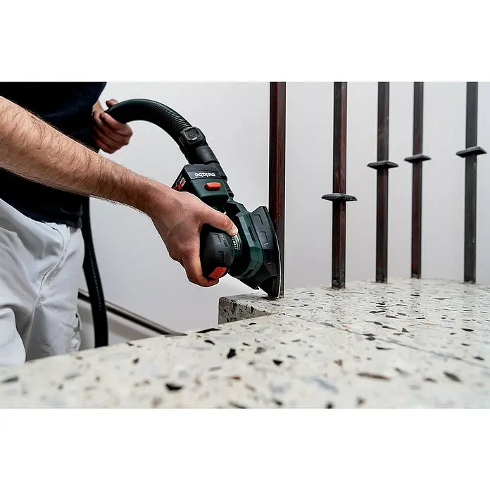 Metabo Akku-Multischleifer PowerMaxx SMA 12 BL - 12 V, Ohne Akku, Breite Schleifplatte: 100 mm, Länge Schleifplatte: 150 mm - Ein Mann schleift mit einem Metabo Winkelschleifer eine Treppenstufe aus Terrazzo, wobei er den Schleifstaub absaugt.
