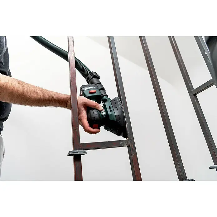 Metabo Akku-Multischleifer PowerMaxx SMA 12 BL - 12 V, Ohne Akku, Breite Schleifplatte: 100 mm, Länge Schleifplatte: 150 mm - Eine Person schleift mit einem Metabo-Schleifgerät ein Eisengeländer ab. Das Gerät ist grün und schwarz und hat einen Absaugschlauch.