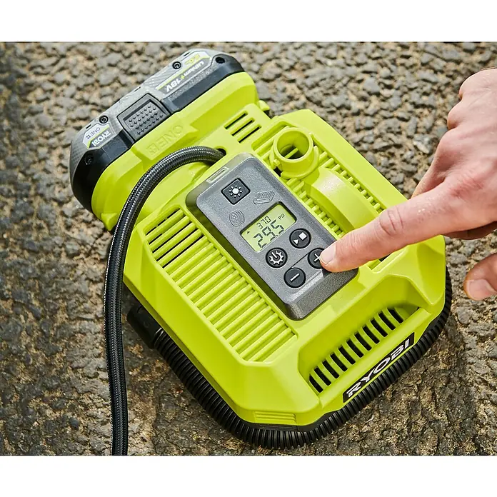 Ryobi ONE+ Akku-Kompressor RMI18-0 - 18 V, 11 bar - Nahaufnahme eines Ryobi ONE+ Akku-Luftkompressors mit digitaler Steuerung, der auf einer rauen Oberfläche liegt und von einer Hand bedient wird.