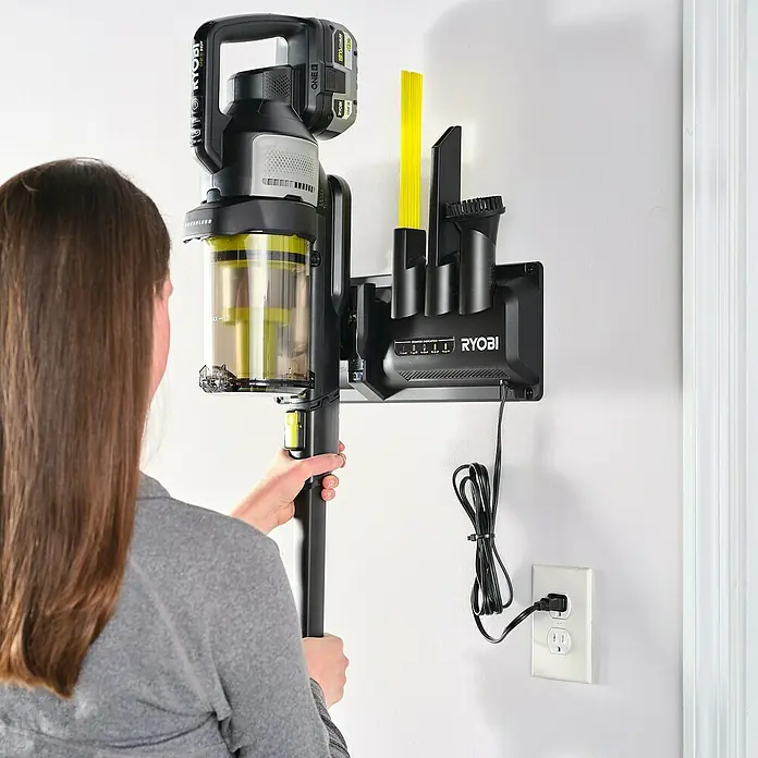 Ryobi ONE+ Wandhalterung mit Ladefunktion - Passend für: Ryobi Akku-Bodenhandsauger RASV18BL-0 - Ein Ryobi Akku-Staubsauger mit Wandhalterung und Ladefunktion wird von einer Person bedient. Das Gerät ist schwarz und gelb.