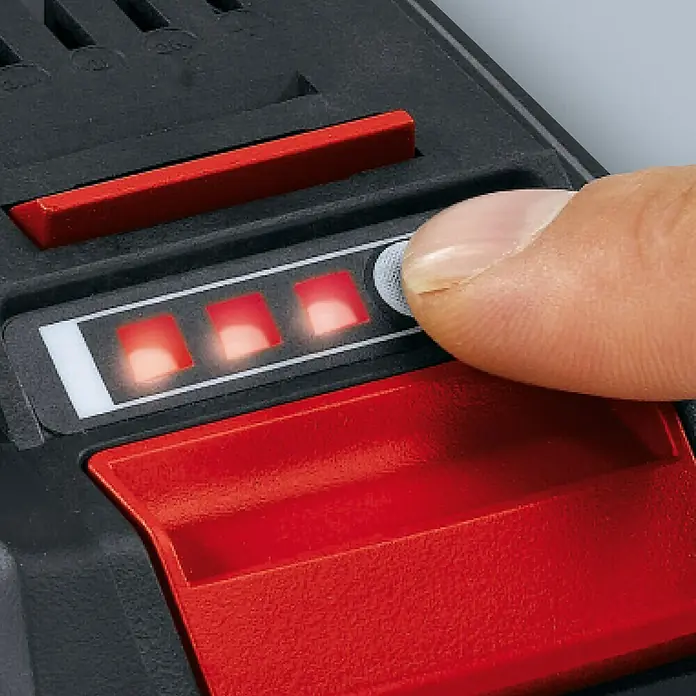 Einhell PXC 18V Batería - 4 Ah - Primer plano de una batería Einhell con un indicador rojo que muestra el nivel de carga, mientras un dedo presiona un botón para activar la pantalla.