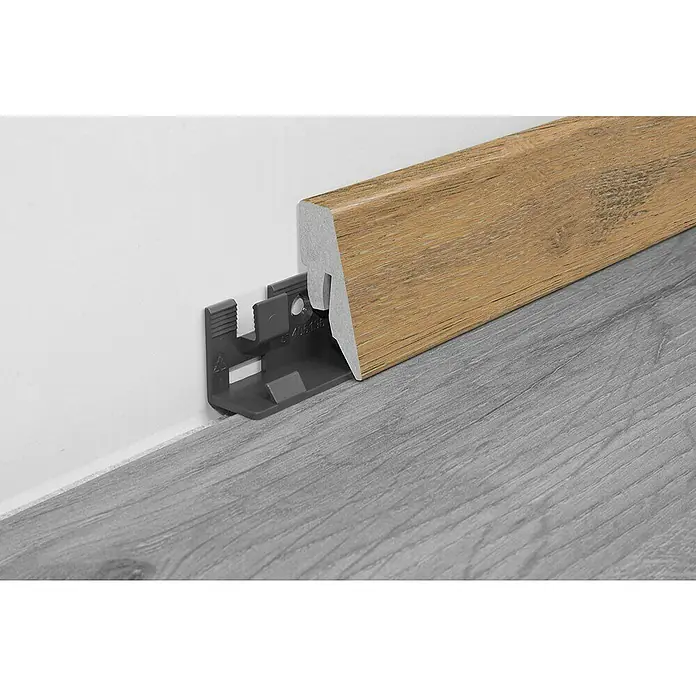 LOGOCLIC Sockelleiste Sockelleiste K40 C Eiche Tegen - L x B x H: 260 x 19 x 40 mm, MDF, Eiche Tegen - Nahaufnahme einer Holzfußleiste mit grauem Untergestell auf einem grauen Laminatboden vor einer weißen Wand.
