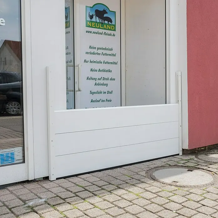 Masys Hochwasser-Kit Large - 200 x 60 cm - Weißer Hochwasserschutz vor einem Schaufenster mit Werbung für Neuland Fleisch, der den Eingang vor Wasserschäden schützt.