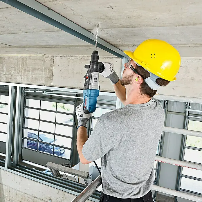 Bosch Professional Kombihammer GBH 2-28 F - 880 W, 3,2 J, SDS-Plus-Aufnahme, Inkl. 3 x Bohrer & Meißel - Bauarbeiter mit Boschhammer beim Bohren in eine Betondecke, ausgerüstet mit Helm und Schutzbrille.