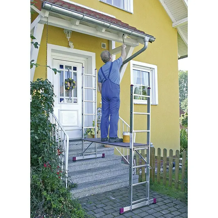 Krause Corda Leitergerüst - Arbeitshöhe: 4,05 m, Anzahl Tritte: 14 Stk., Belastbarkeit Gerüst: 150 kg/m² - Mann streicht Dachrinne von Aluminium-Rollgerüst auf Steintreppe vor gelbem Haus. Das fahrbare Gerüst ist leicht zu verstellen und anzupassen.