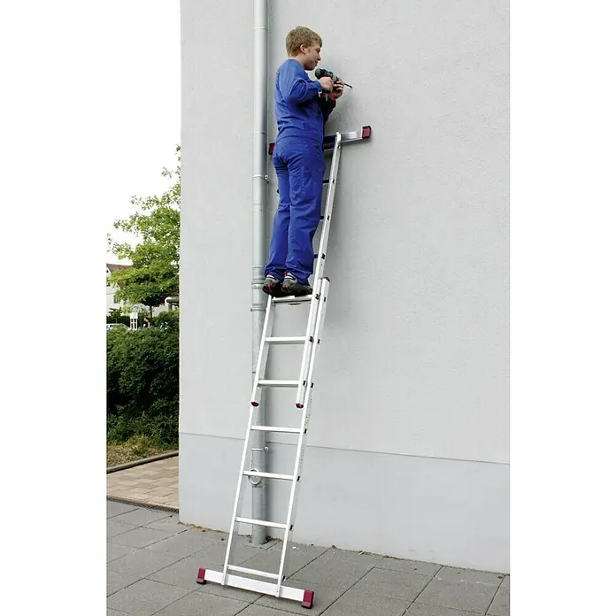 Krause Corda Leitergerüst - Arbeitshöhe: 4,05 m, Anzahl Tritte: 14 Stk., Belastbarkeit Gerüst: 150 kg/m² - Ein Mann auf einer Mehrzweckleiter bohrt in eine weiße Wand im Freien, die Leiter ist durch eine Regenrinne gestützt.