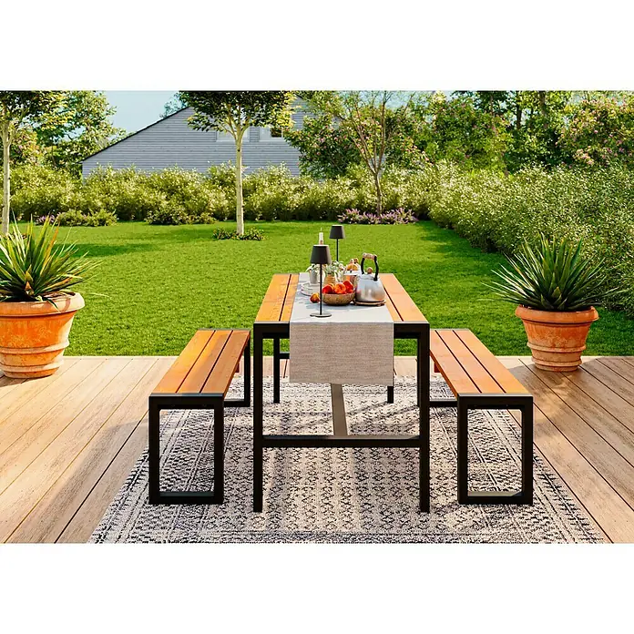 Promadino Gartenmöbel-Set Sylt - 3 -tlg., Kiefernholz, Braun/Schwarz - Einladender Outdoor-Essbereich mit einem stilvollen Holztisch mit Bänken, perfekt für Mahlzeiten im Freien, umgeben von üppigem Grün und Pflanzen.
