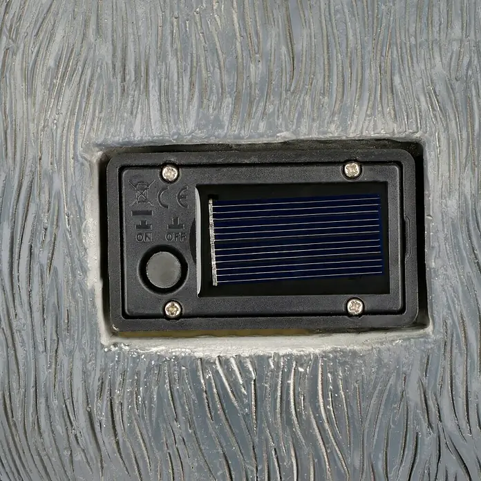 BAUHAUS Solar-Dekoleuchte - Lichtfarbe: Warmweiß, 29,5 x 25 x 35 cm, Waschbär - Nahaufnahme des Solarpanels mit Ein-/Ausschalter an einer grauen Oberfläche. Es lädt das Produkt mit Sonnenenergie auf.