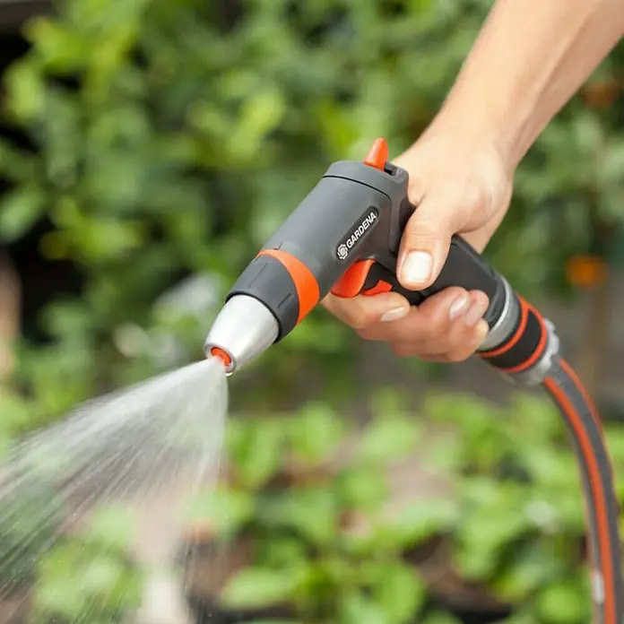Gardena Premium Reinigungsspritze - Anzahl Sprühformen: 3 Stk., Metall/Kunststoff - Nahaufnahme einer Hand, die eine Gardena-Gartenspritze hält, aus der Wasser spritzt, ideal für die Gartenbewässerung.
