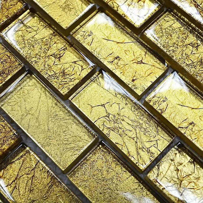 Mosaikfliese Brick Crystal Uni XCM 8GO35 - 30 x 30 cm, Gold, Glänzend - Nahaufnahme von goldenen Glasmosaikfliesen in einem eleganten Fischgrätmuster, das Luxus und Wärme ausstrahlt.