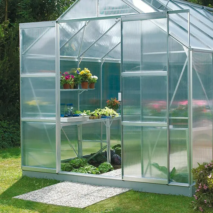 Vitavia Gewächshaus-Türerweiterung - Aluminium - Ein Gewächshaus aus Glas mit Regalen voller Pflanzen und Gemüse, das eine ideale Umgebung für den Pflanzenanbau bietet.