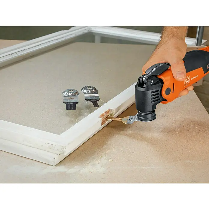 Fein Starlock Plus Hartmetall-Feile - 30 x 10 mm - Nahaufnahme eines Fein Multimaster-Werkzeugs beim Schneiden eines Holzrahmens. Zusätzliche Klingen liegen daneben.