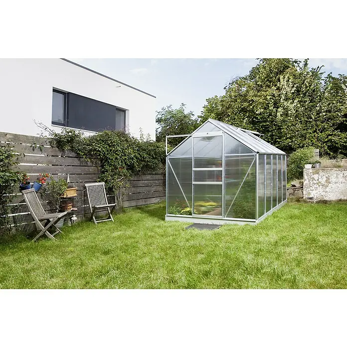 Vitavia Gewächshaus Venus 6200 Plus - Außenmaß inkl. Dachüberstand (B x T): 195 x 321 cm, 4 mm, Aluminium - Ein Gewächshaus aus Metall und Kunststoff steht in einem gepflegten Garten mit grünen Rasenflächen und einer Holzwand.