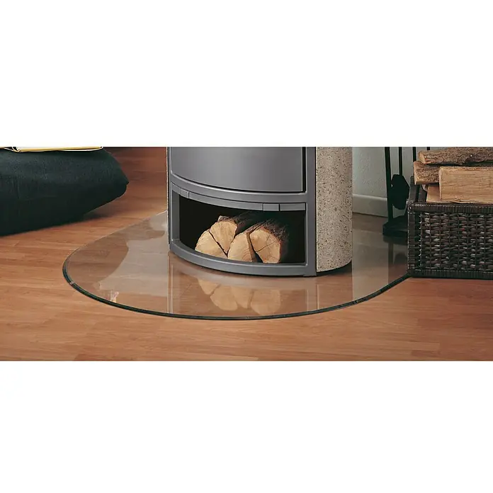 Justus Glasbodenplatte B3 - 120 x 100 cm, Gebogen - Ein grauer Kaminofen mit Holzlagerung auf einer runden Glasplatte, umgeben von Holzboden und einem Korb mit Holz.